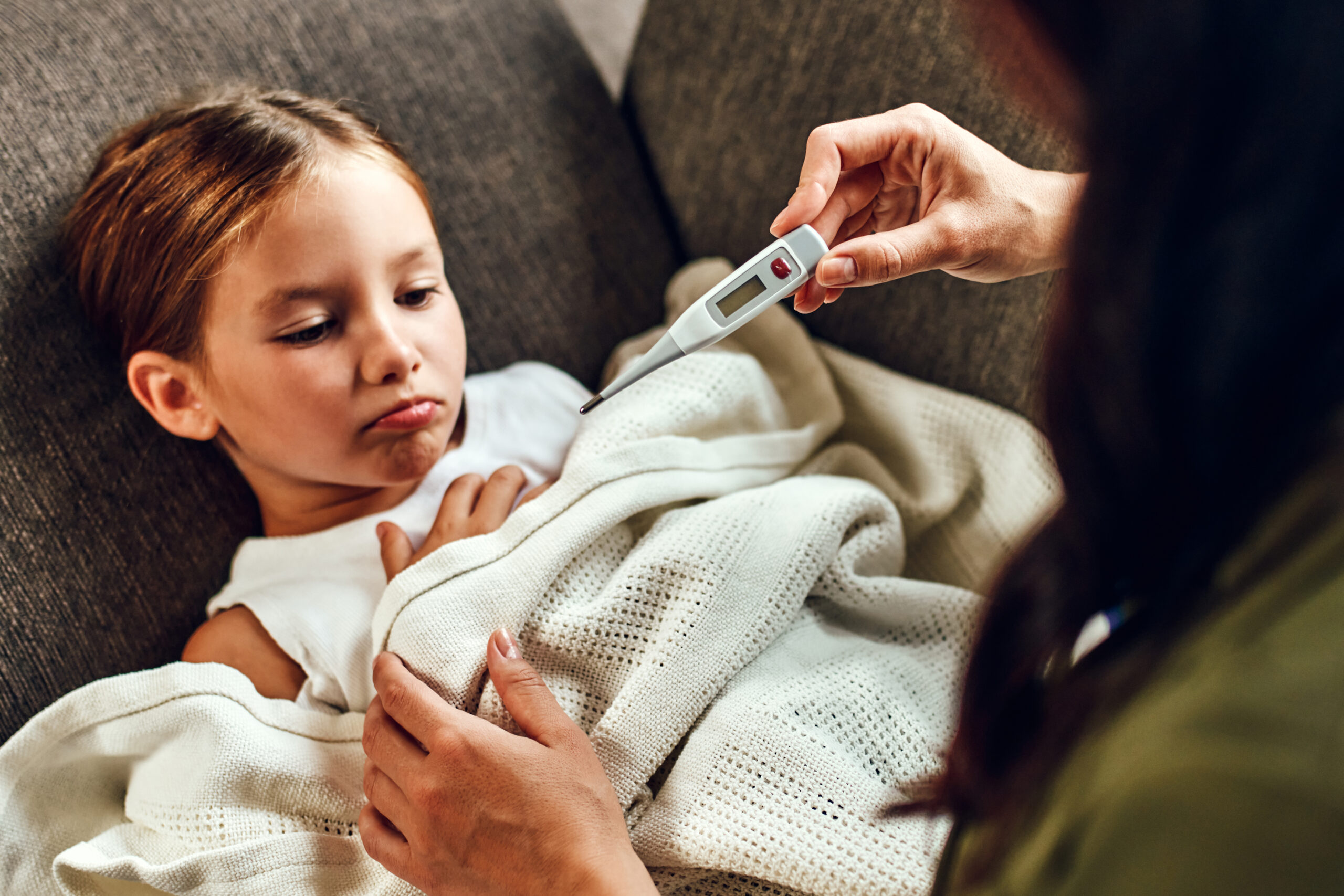 The child has a high fever. Mom looks at the thermometer, measures her daughter's temperature.