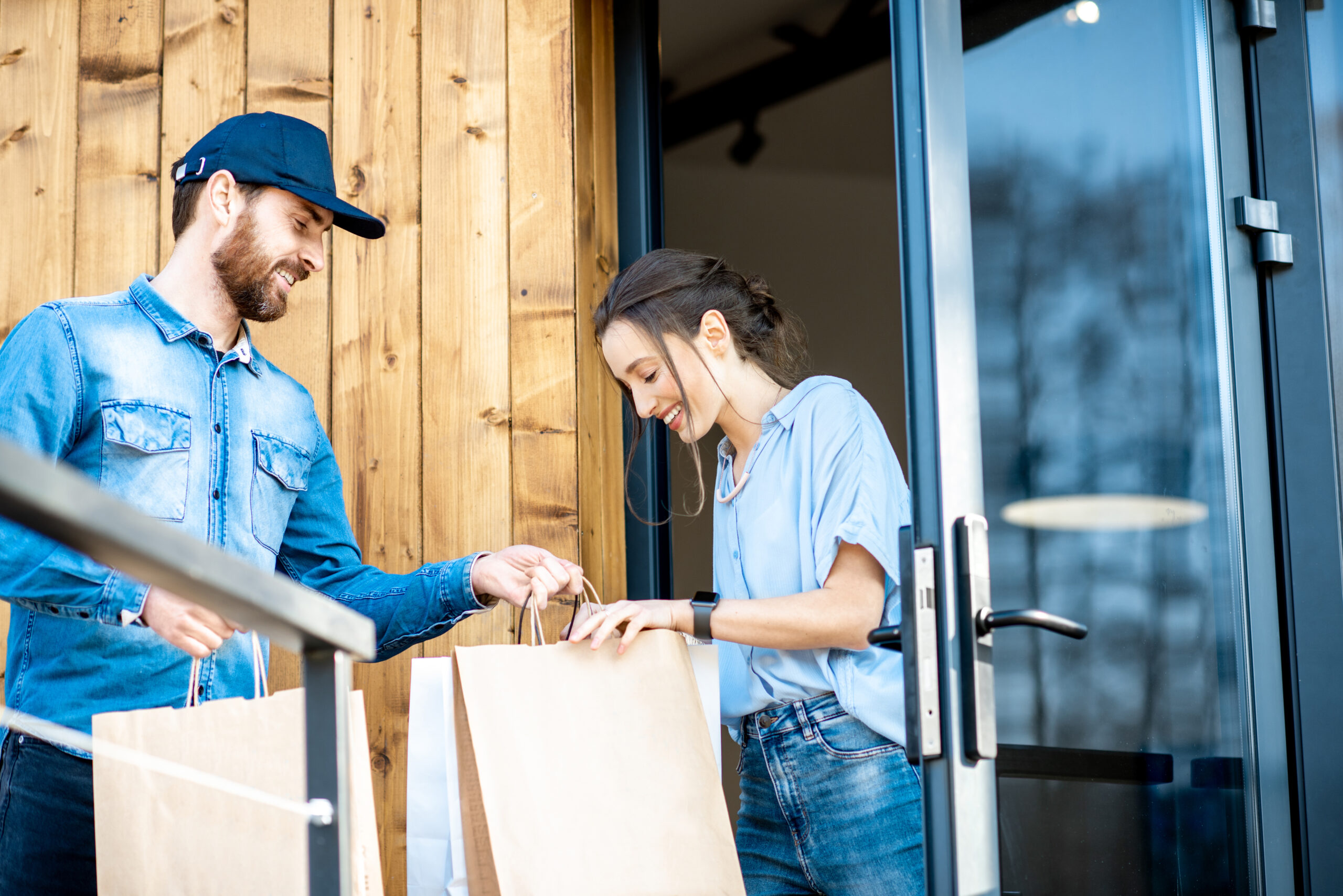 Delivery man bringing some goods packaged in paper bags for a young woman client to home. Buying clothes online and delivery concept