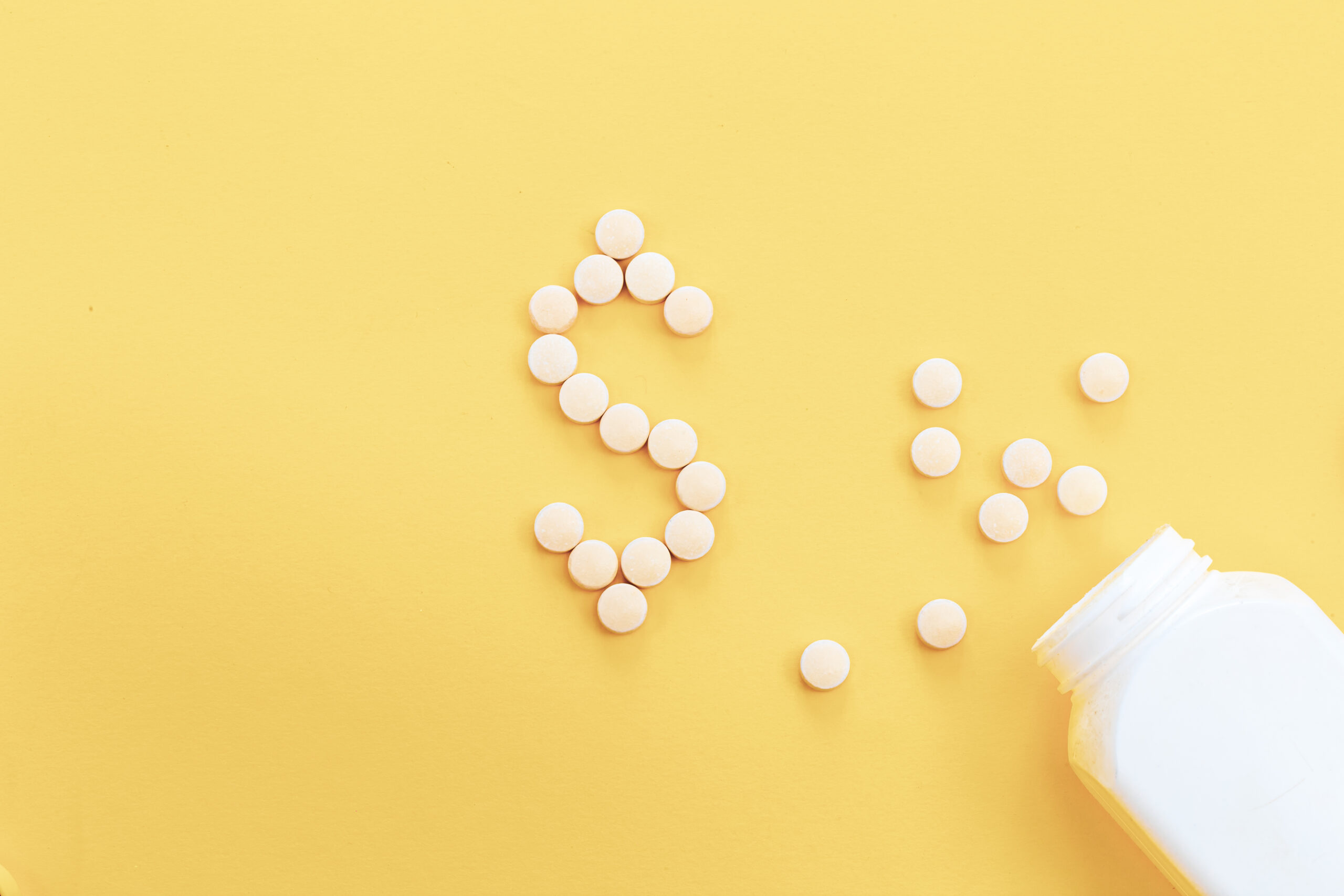 Pills laid out in the shape of a dollar on a yellow background, flat lay, conceptual minimalism.