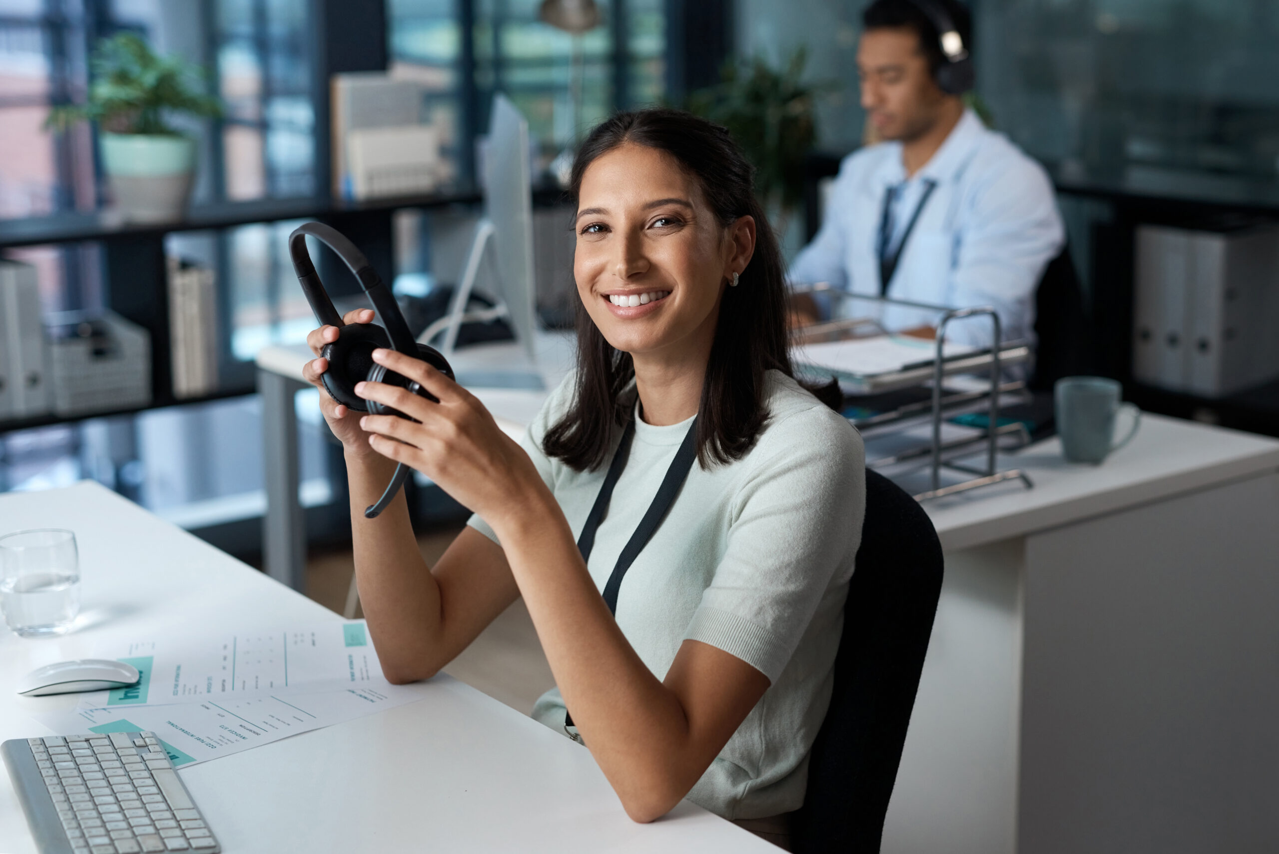 Portrait of a young woman using a headset and computer in a modern office.