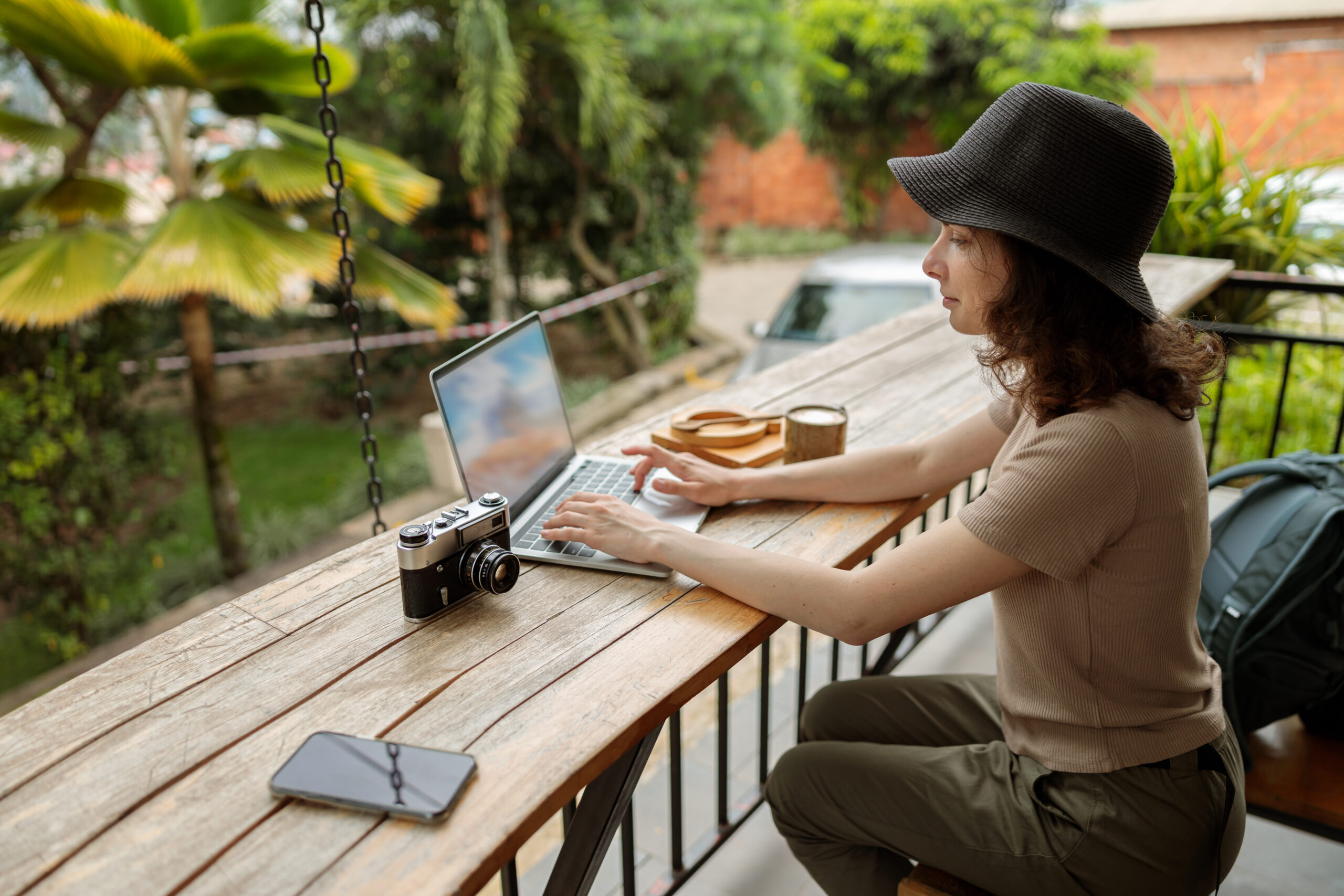 Smiling woman using laptop while working online during the journey Side view of happy lady in hat typing on laptop while working online during the journey