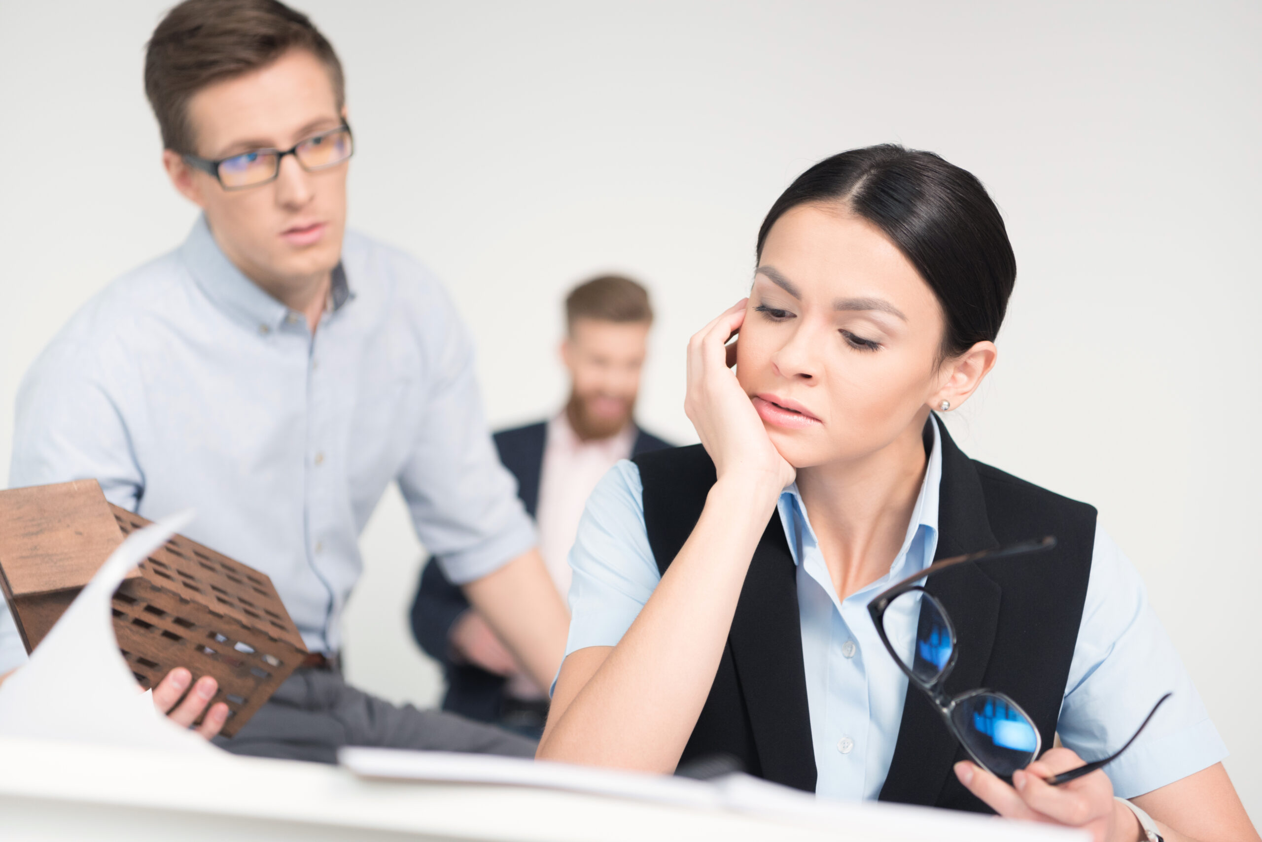 Tired young businesswoman sitting at table with eyeglasses near male coworker